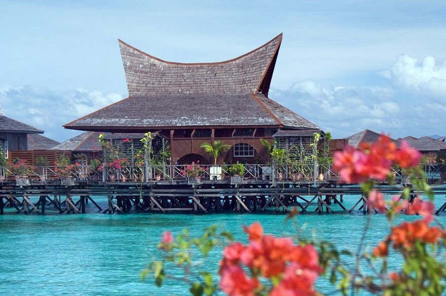 隔着九重葛花叢望見的婆羅洲別墅套房（Borneo Villa Suite），建於水上，屋頂爲弧形木瓦